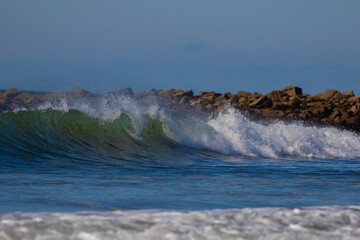 yellowish-white waves against a blue sky and rocks. 