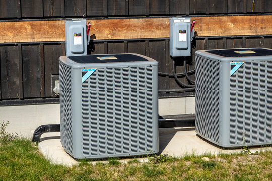 Calgary, Alberta, Canada. Sep 1, 2024. Two Daikin outdoor air conditioning units are installed side-by-side on a concrete pad. The units are grey and have black grilles.