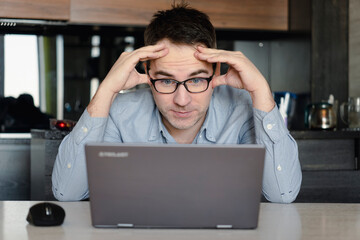 man in eyeglasses holding laptop and looking extremely perplexed on home backdrop.
