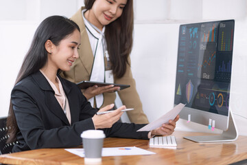 Two Asian young businesswomen working on computer with analyzing financial charts in the modern office, Business financial documents and planning idea project concept.