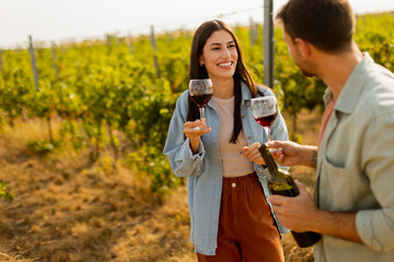 A joyful couple enjoying wine tasting together in a sunny vineyard during the golden hour,...