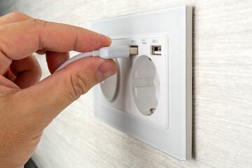 Man hold USB plug against wall charger. Plug-in connector into european wall outlet or socket with AC adapter. Unplugging USB cable from power adapter. Disconnect USB cord from the cellphone charger.