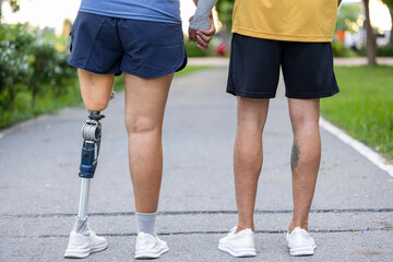Couple with prosthetic leg from amputation walking exercise in the public park together for disability and handicap people and diversity with universal design for better accessibility infrastructure