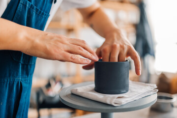 Close up of creative female artisan's hands shaping clay mug at studio