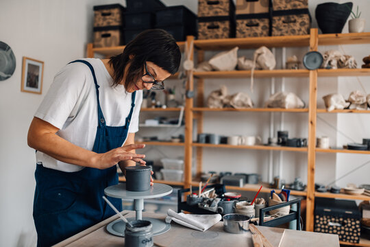 A precise female potter making earthenware at pottery workshop.