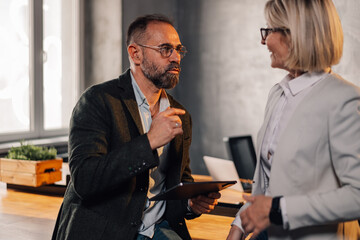 Mature businesspeople at modern office discussing project on a tablet.