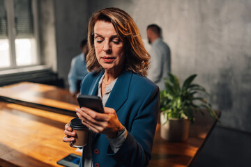 Close up of mature leader using cellphone at office during meeting.