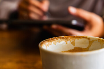 empty coffee cup with latte art residue, with a person writing on a tablet in the background