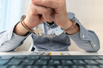 man in handcuffs is sitting at his workplace with a computer and money in dollars.. The concept of...