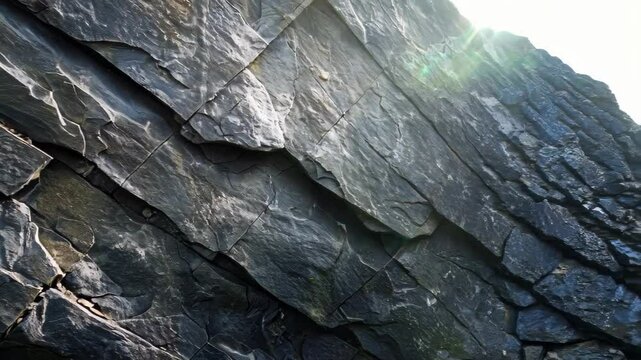 A close-up of a layered slate stone wall highlights its natural textures and earthy tones. Soft sunlight enhances the stone's rugged beauty, ideal for decor and landscaping.