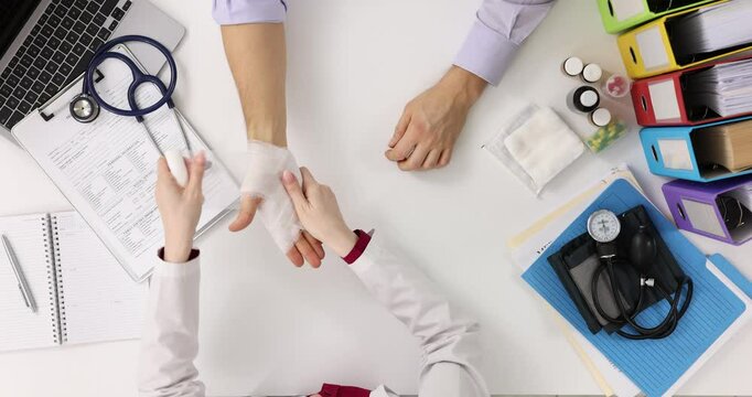 Taumatologist bandages patient sore arm in clinic, top view