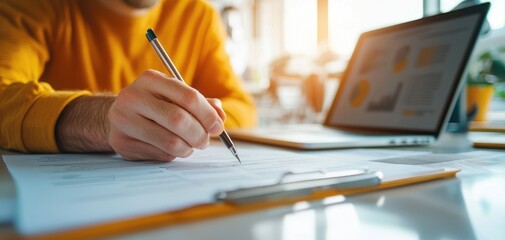 Close-up of hands writing on a business plan with a laptop in the background, startup strategy