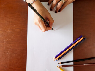 hand holding colored pencils on white background. and paint it on the table using a piece of paper