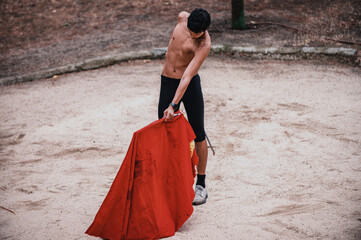 Front view of a young adult bullfighter practicing performance holding his red cloak with one hand