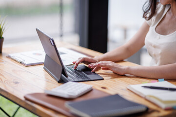 Businesswomen or Asian Accountants using calculator and a tablet laptop computer to analyze business report graphs and finance charts at the workplace, financial and investment concept.
