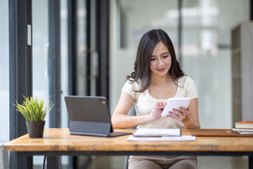 Fototapeta premium Businesswomen or Asian Accountants using calculator and a tablet laptop computer to analyze business report graphs and finance charts at the workplace, financial and investment concept. 