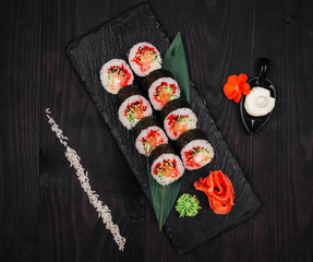 Sushi rolls set served on black stone slate on dark wooden table