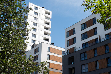 Modern apartment buildings with white and brown facade seen from below, surrounded by trees