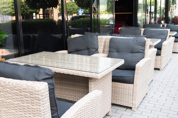 Outdoor cafe seating with wicker furniture and glass table in front of large windows