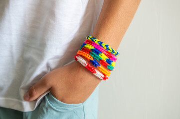 Child wearing colorful loom band bracelets on wrist with hand in pocket.