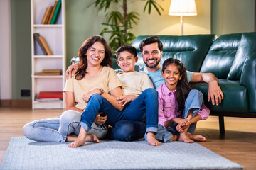 Happy Indian Asian family sitting on the floor with kids in arms, enjoying family time in new home