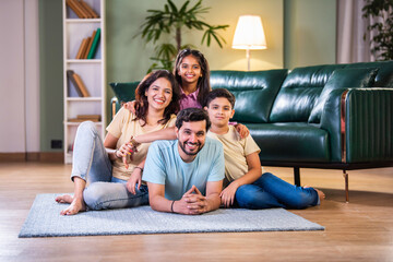 Happy Indian family enjoying quality time at home with father on floor, kids sitting on his back