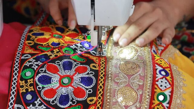 stitching the traditional kanch kachhi and golden laces on the chaniya choli for garba in navratri. closeup to sewing machine with the borders getting stitched on the fabric. indian ethnic attire