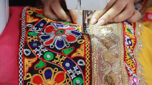 stitching the traditional kanch kachhi and golden laces on the chaniya choli for garba in navratri. closeup to sewing machine with the borders getting stitched on the fabric. indian ethnic attire