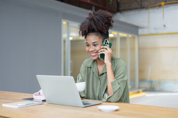 African American young woman using smartphone with laptop computer.