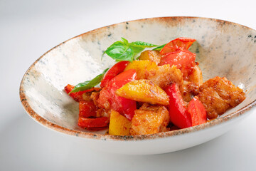 A dish with fried or stewed vegetables, ratatouille or caponates with potatoes, sweet peppers and tomatoes in a plate on a white background, close up