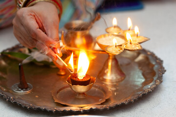 Puja or Arti thali with a brass oil lamp. An Indian woman lights a (Dhup) incense stick to worship the Hindu God.