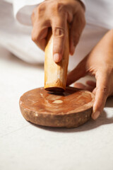 An Indian man is rubbing a sandalwood stick to make sandalwood paste, commonly used in traditional Indian pooja rituals.
