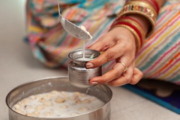 An Indian woman pours panchamrit into a lota, preparing for prasad distribution on the occasion of 'Krishna Janmashtami'.