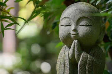 Obraz premium Jizo, the Protector of Children, in Peaceful Meditation: A Stone Statue Surrounded by Lush Greenery.