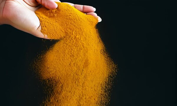 Hand pouring turmeric powder on black background, slow motion. 4K Video