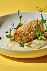 A classic Ukrainian dish, Chicken Kiev, is beautifully presented on a white plate against a vibrant yellow background. The crispy, golden-brown chicken cutlet, stuffed with garlic butter