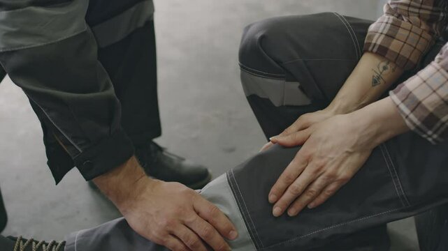 Factory worker helping female colleague with leg injury supporting her and calling for doctor via walkie-talkie