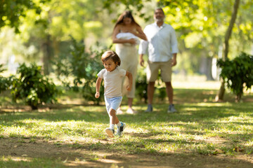 Fototapeta premium Little boy running ahead of family walking in park