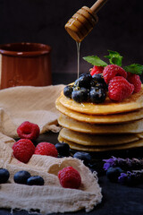 pancakes with berries and honey on dark background