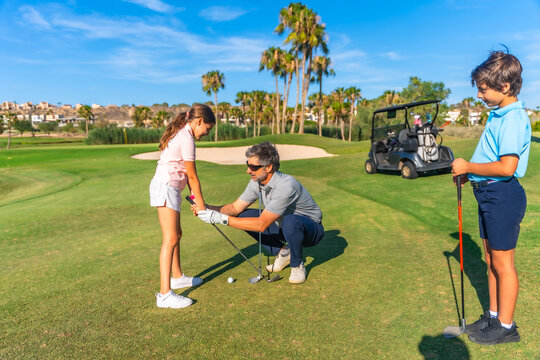Coach teaching a girl and her brother to play golf