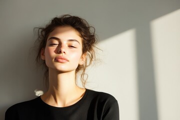 Modern Greek Fashion Model Gracefully Poses Against Soft Light Gray Wall with Calm Expression and Selective Sunlight Shadows