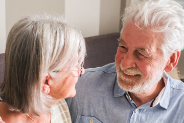 Heartwarming moment of an elderly couple sitting on a cozy sofa at home, smiling and sharing tender words. Captures the essence of mature love, mutual care, and the happiness of togetherness in late