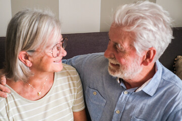 Mature couple sitting on a sofa, lovingly gazing at each other with affection, enjoying their time together at home. Capturing the essence of senior lifestyle, enduring relationships, and love in old