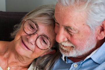 Close-up of an elderly couple embraced and happy on the sofa at home, both with dreamy and relaxed expressions. They enjoy their long-lasting love and friendship, showcasing mature, healthy, 