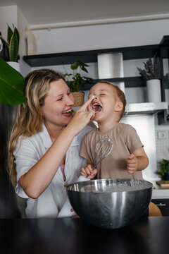 Playful mother and son preparing whipped cream in kitchen at home