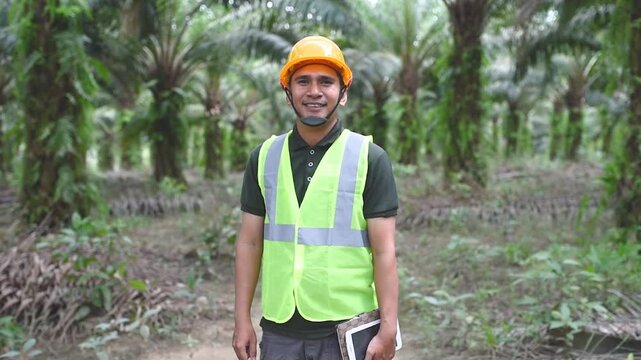 Slow motion video of a field worker palm oil is standing and smiling at the camera, wearing a safety worker