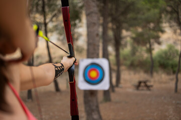 Athlete woman with bow and arrow aiming on sport target board at forest