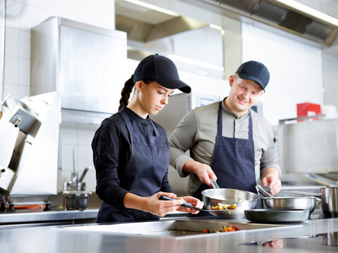 Trainee cooking meal with chef in restaurant