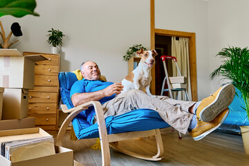 Senior man resting on rocking chair with dog in new apartment