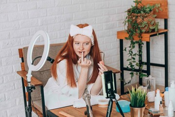 Teenage girl beauty blogger recording a makeup tutorial at home.